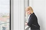 Mature businesswoman leaning and staring through office window