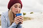 Young woman blowing into cup of coffee on cold day