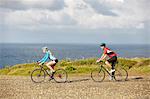 Cyclists riding on gravel road overlooking ocean