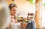 Young woman relaxing on garden patio eating salad