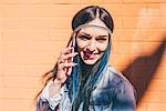 Young woman with dip dyed blue hair talking on smartphone in front of orange wall