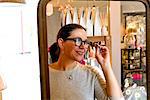 Mirror image of mature female customer trying on spectacles in gift shop