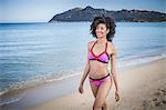 Beautiful young woman wearing pink bikini strolling on beach, Costa Rei, Sardinia, Italy