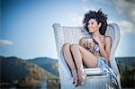 Beautiful young woman wearing bikini top and sarong sitting on wicker chair, Costa Rei, Sardinia, Italy