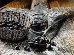 Juniper berries in small glass jar, metal vintage spoon and woven basket, rustic wooden chopping board