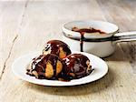 Profiteroles with hot chocolate sauce on white plate, rustic wooden table
