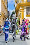 Cuba, Havana, Habana Vieja.  Colourful stilt walkers march down a street in Habana Vieja.