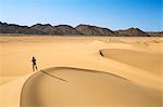 Niger, Agadez, Sahara Desert, Tenere, Kogo. A visitor photographs beautiful sand dunes in the Tenere with the Taghmert Mountains in the distance.