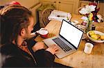 Couple using laptop while sitting at breakfast table