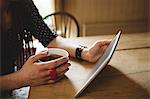 Midsection of woman using tablet while having coffee at home