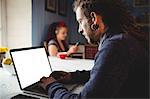 Man using laptop while woman sitting in background at home