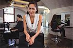 Portrait of smiling female hair dresser leaning on chair at salon