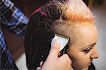 Woman getting her hair trimmed with trimmer in barber shop