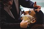 Man getting his beard shaved with shaving brush in barber shop