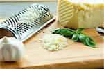 Heap of grated Parmesan on wooden background with leaf of basilic,garlic and  with grater.Close up shot