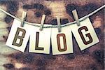 The word "BLOG" stamped on cards and pinned to an old piece of twine over a rusted metal background.