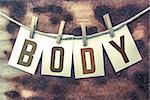 The word "BODY" stamped on cards and pinned to an old piece of twine over a rusted metal background.