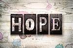 The word "HOPE" written in vintage dirty metal letterpress type on a whitewashed wooden background with ink and paint stains.