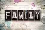 The word "FAMILY" written in vintage, dirty metal letterpress type on a whitewashed wooden background with ink and paint stains.