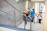 Young female student sliding down stairway handrail at higher education college