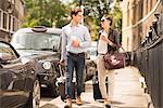 Young businessman and woman walking with wheeled suitcase on city street, London, UK