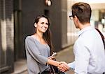 Young businessman and businesswoman shaking hands outside office, London, UK