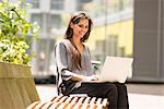 Businesswoman typing on laptop on park bench, London, UK