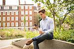 Businessman reading smartphone texts in city, London, UK