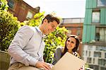 Young businesswoman and man using laptop outside office, London, UK