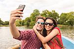 Young couple taking smartphone selfie in rowing boat in Regents Park, London, UK