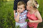 Girl whispering in brothers ear in meadow