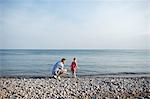 Mid adult man and daughter skimming stones at Lake Ontario, Oshawa, Canada