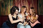 Three adult female friends raising a glass whilst sitting in bar