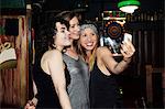 Three adult female friends taking smartphone selfie on night out in bar