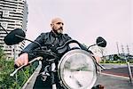 Mature male motorcyclist sitting on motorcycle on city road