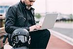 Mature male motorcyclist on roadside using laptop