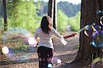Rear view of woman in forest making bubbles with bubble wand