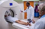 Doctor looking at brain mri scan on digital tablet and patient entering mri scan machine at hospital