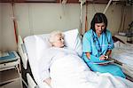 Nurse interacting with senior patient while looking at report in hospital