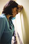 Depressed nurse leaning against wall in hospital