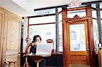 Young woman sitting in cafe, drinking coffee, using laptop