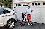 Portrait of senior male golfer standing next to garage door with golf bag