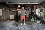 Portrait of senior man standing in garage holding broom