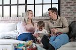 Mother and father sitting on sofa with toddler, toddler holding digital tablet