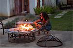 Mature woman crouching in front of patio fire at dusk
