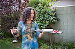 Mature woman holding cutting board and red wine at garden party