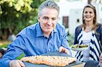 Mature man holding chopping board with fish cuisine at garden party