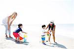 Two mothers and baby sons playing with beach ball and pinwheel on beach, Malibu, California, USA