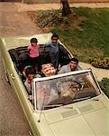 1970s AFRICAN AMERICAN FAMILY OF FOUR SEATED IN CONVERTIBLE CAR FATHER MOTHER SON DAUGHTER LOOKING AT CAMERA