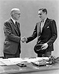 1930s TWO MEN STANDING AT DESK IN OFFICE SHAKING HANDS